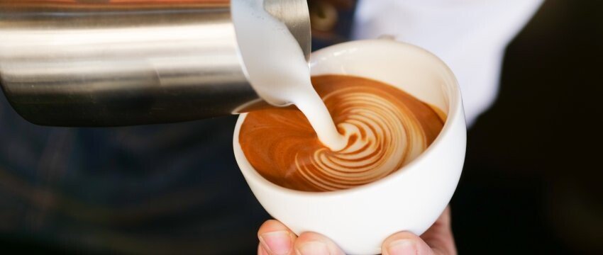 Frau lässt Milch in eine Cappuccinotasse fließen